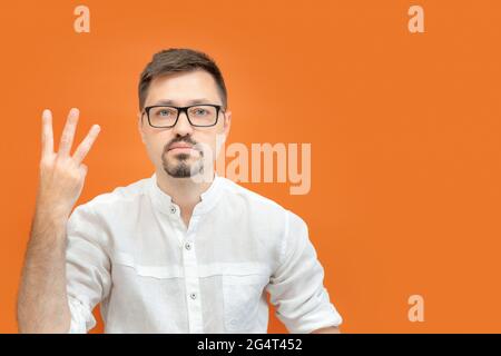 Handsome serious confident business man wearing nerd glasses over orange background showing and pointing up with fingers number three. Stock Photo