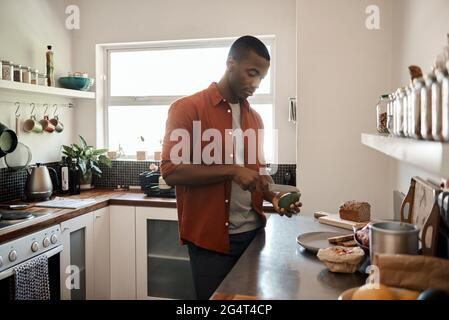 Young African man cutting an avocado in his kitchen Stock Photo