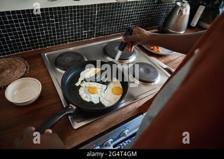 Young African man frying eggs on his stove for breakfast Stock Photo