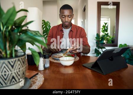 Young African man using a tablet and eating breakfast Stock Photo