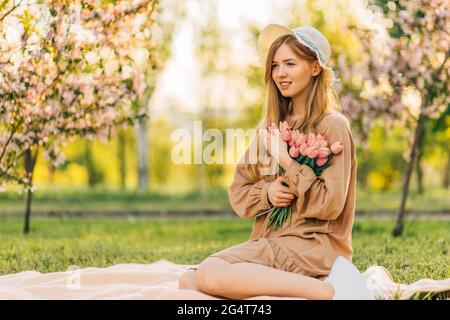 Beautiful smiling young woman, with a bouquet of tulips, on the lawn in the park, on a summer sunny day, enjoying nature Stock Photo