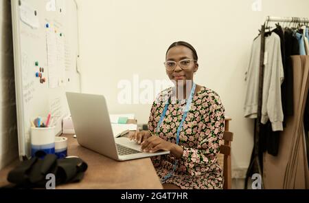 Smiling African female fashion designer working on laptop in her studio Stock Photo