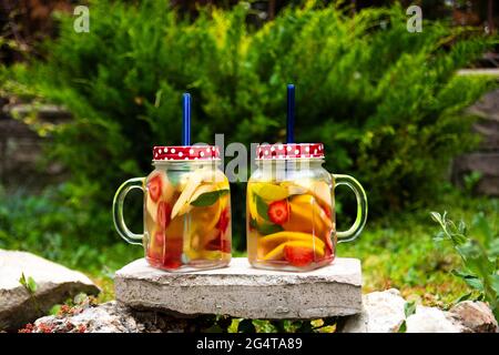 Two Jars of glass, delicious detox drink with red, orange and yellow fruits, standing on the Stone. Selective Focus Glasses. Stock Photo