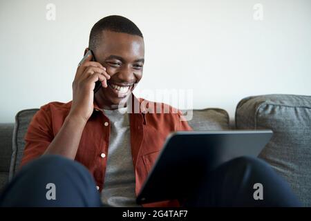 African man talking on his phone and laughing while working from home Stock Photo