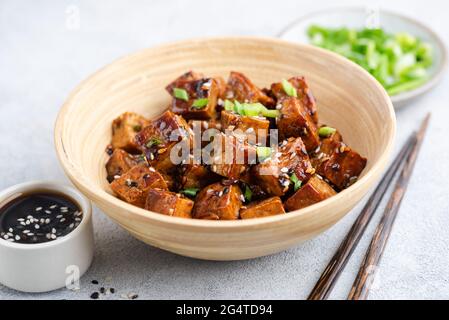 Tofu cubes in sweet teriyaki sauce with sesame seeds and scallions in bamboo bowl Stock Photo