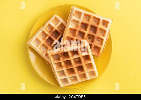 Sweet belgian waffles on yellow plate, isolated on yellow background, Table top view Stock Photo