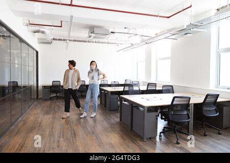 Casually dressed young man and woman looking for premises to rent for start up business walking into empty modern open plan office Stock Photo