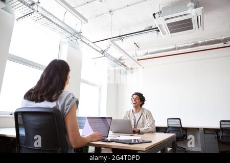 Casually dressed young man and woman working on laptops at desks in modern open plan office Stock Photo