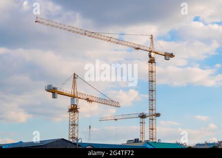Three yellow tower construction cranes against cloudy sky Stock Photo
