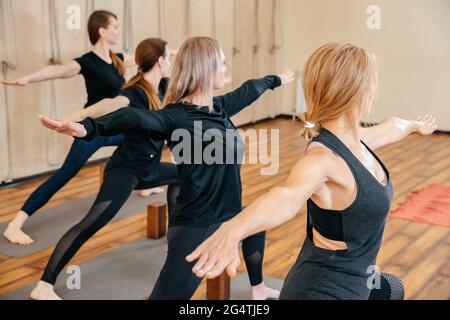 Group of four women standing in a row practicing yoga in yoga studio Stock Photo