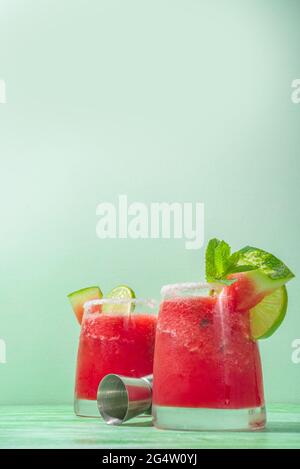 Cold summer cocktail, watermelon margaritas or mojito with watermelon and lime slices, crushed ice and mint. Seasonal refreshing drink, on bright gree Stock Photo
