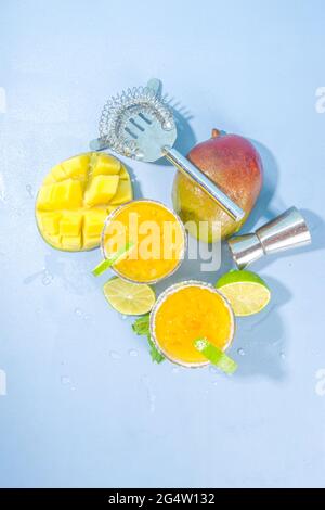 Cold summer cocktail, mango margaritas with tequila, salt lime slices, crushed ice and mint. Seasonal refreshing drink, on bright blue sun lighted bac Stock Photo