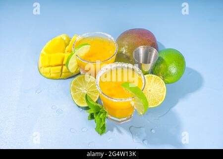 Cold summer cocktail, mango margaritas with tequila, salt lime slices, crushed ice and mint. Seasonal refreshing drink, on bright blue sun lighted bac Stock Photo