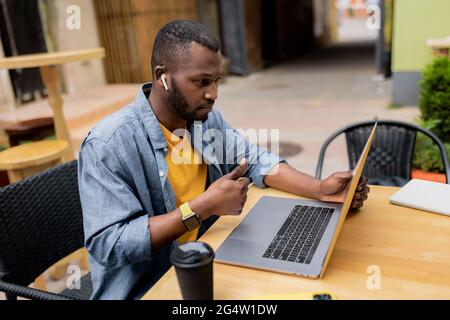 Young attractive bearded male in wireless headphones showing approval gesture thumb up and discussing talking with work colleagues or teacher through Stock Photo