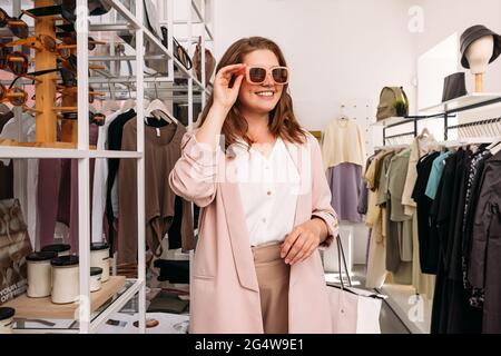 Happy plus size woman standing in small fashion store. Cheerful female buyer wearing sunglasses in a boutique. Stock Photo