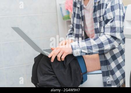 buisnessman sit on toilet and work with laptop in bathroom Stock Photo