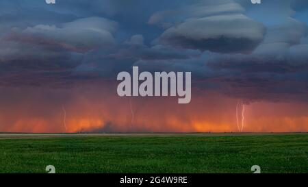 Multiple lightning bolts strike along the Colorado / Wyoming border at sunset with the orange glow of sunset seen on the horizon Stock Photo