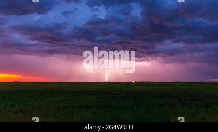 Lightning bolt strikes at dusk on the Wyoming / Colorado border with dark storm clouds overhead. The orange glow of sunset is seen on the horizon. Stock Photo