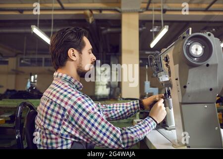 Young man working on an industrial sewing machine at the workshop of a shoe factory Stock Photo