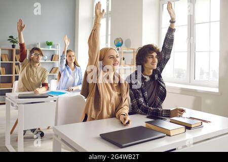 High school teenager student raising hands sitting at desk in classroom Stock Photo