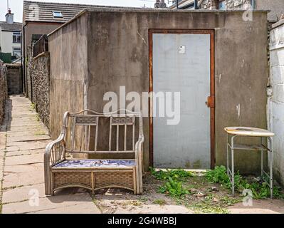 Old rattan seat and table discarded in town back street Stock Photo