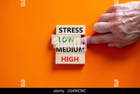 Low or high stress level symbol. Businessman chooses the wooden block with words low stress. Words stress low medium high. Beautiful orange background Stock Photo