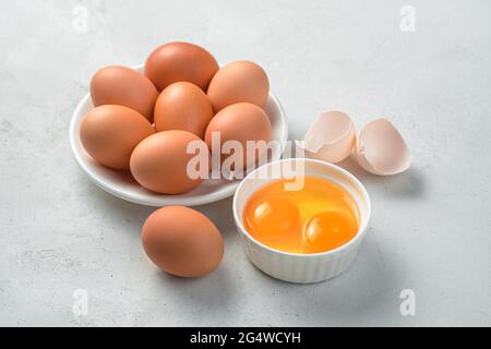 Raw chicken eggs and two yolks on a gray background. Side view, close-up. Stock Photo