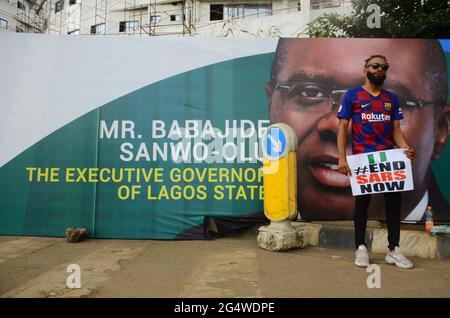 A youth protester of ENDSARS displaying his placards in front of a banner with the picture of the Lagos State Governor (Babajide Sonwo-Olu) at the ongoing protest against the harassment, killings and brutality of the Nigerian Police Force Unit called Special Anti-Robbery Squad (SARS) in the Lagos State House of Assembly. Lagos, Nigeria. Stock Photo