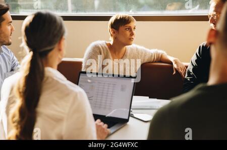 businesswoman thinking during discussion of future strategy in meeting with team. Female executive in meeting with colleagues. Stock Photo