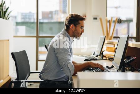 Executive looking at computer screen and typing on keyboard in office. Young man sitting in office working on computer. Stock Photo