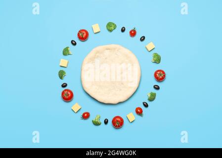 Making vegan pizza with vegetables and vegetarian cheese, isolated on blue-colored background. Flat lay, pizza dough and topping ingredients aligned Stock Photo