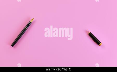 Top down view - black fountain ink pen with gold nib, opened, cap on the right, pink background, space for text. Stock Photo