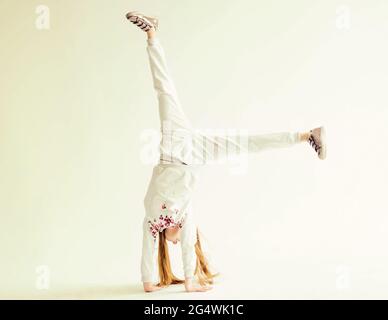Active little girl in grey sport clothes doing a handstand on white background Stock Photo