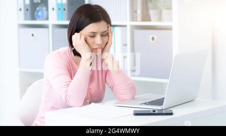 Tired woman at workplace in light office Stock Photo