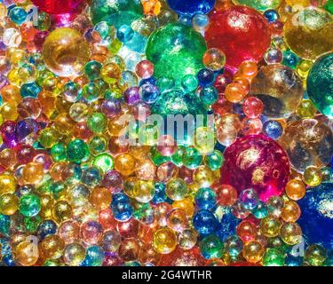 Water beads of different sizes and colors, with gold powder dusting them gathered together under the summer sunlight Stock Photo