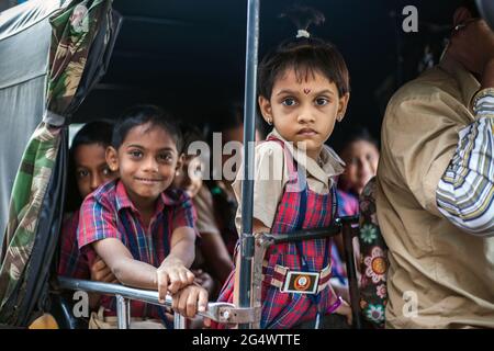 Cute young Indian schoolkids wearing check uniforms on school run in rear of auto rickshaw, Udupi, Karnataka, India Stock Photo