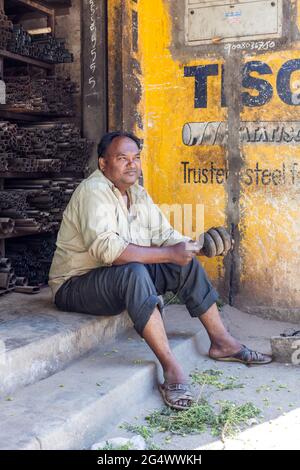 Indian male manual worker sits on step taking break from his workshop, Mysore, Karnataka, India Stock Photo