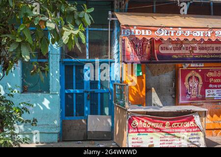 Religious stall and advertising beside blue painted door on light blue wall, Trichy, Tamil Nadu, India Stock Photo