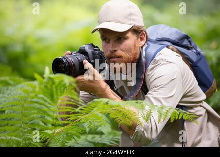 young man trekking among trees and taking pictures Stock Photo