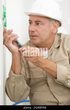 senior electrician using screwdriver on wall socket Stock Photo