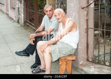 Two old men smiling looking at camera sitting on a bench, Cuban people Stock Photo