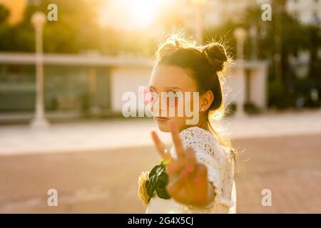 Teenage girl wearing red sunglasses showing peace sign in city Stock Photo