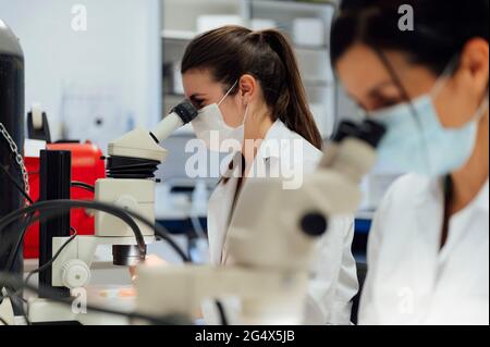 Female scientists looking through microscope while examining medical samples in laboratory during pandemic Stock Photo