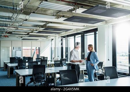 Male and female colleagues discussing while standing by desk in office Stock Photo