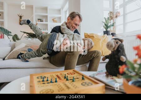 Son playing with father sitting on sofa at home Stock Photo