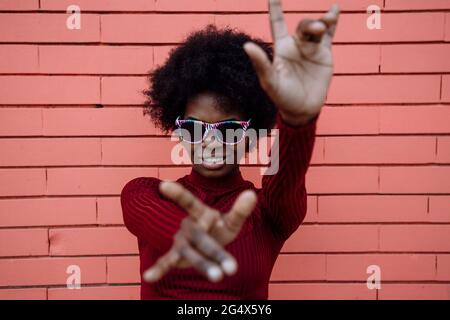 Cool woman with sunglasses making hand signs near brick wall Stock Photo