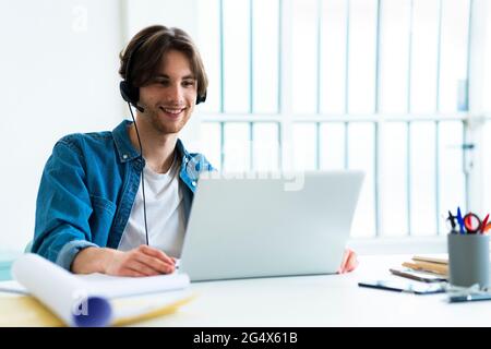 Smiling businessman with headset using laptop while working in office Stock Photo
