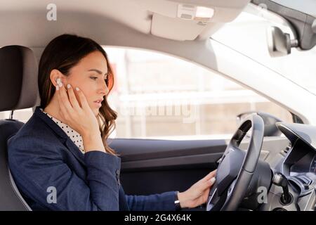 Female entrepreneur talking through in-ear headphones while driving car Stock Photo
