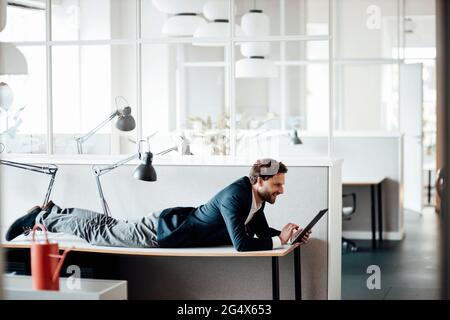 Businessman using digital tablet while lying on table at office Stock Photo