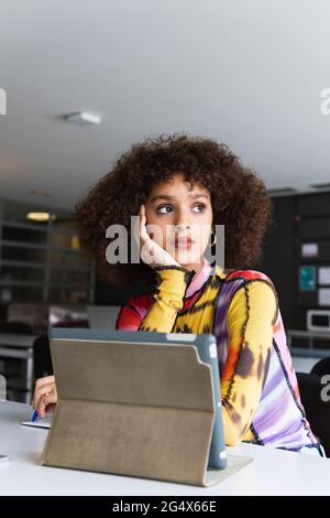 Thoughtful female student with hand on chin looking away in university Stock Photo